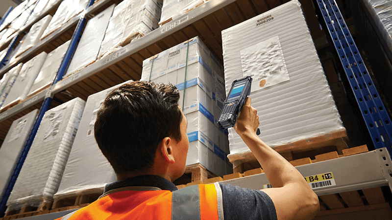 Warehouse worker in a safety vest scanning a pallet label with a Zebra MC9300 mobile computer