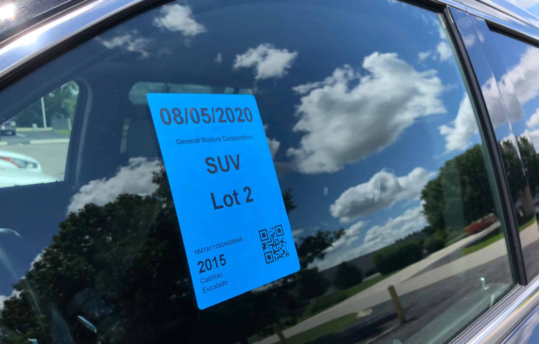 Blue direct thermal lot tag stuck inside a car window showing date, vehicle type, and a QR code