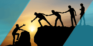 Silhouettes of climbers helping each other up a rock at sunset