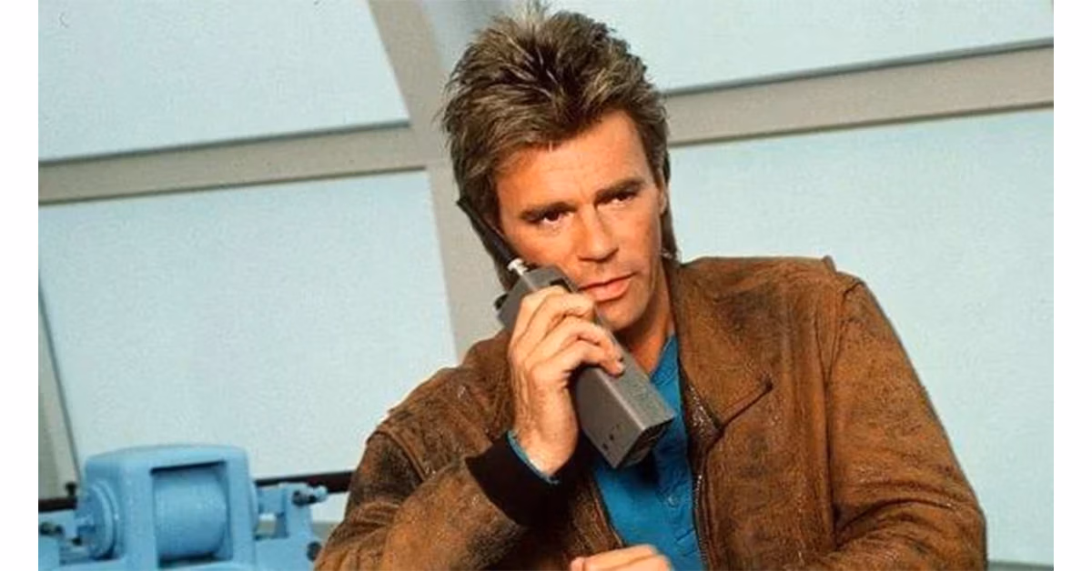 MacGyver holding a handheld radio in a leather jacket