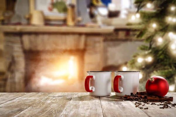 Two red-handled mugs on a wooden table in front of a fireplace and Christmas tree