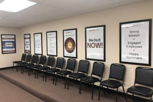 EMP training room with a row of black chairs under framed culture posters including We Do It Now
