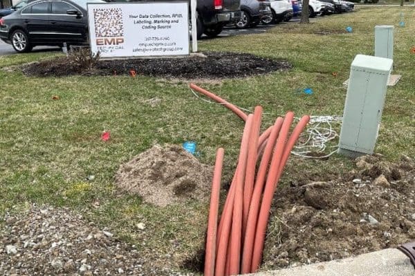 Orange fiber conduit emerging from the ground next to the EMP Technical Group sign and parking lot
