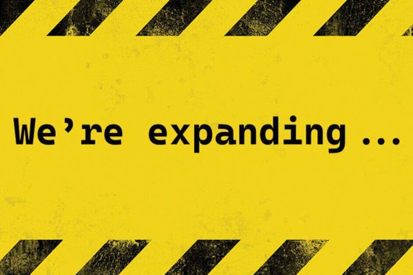 Yellow and black caution-striped sign reading We're expanding