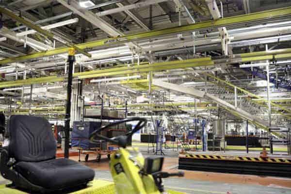 Automotive plant floor with overhead conveyors and a yellow lift seat in the foreground