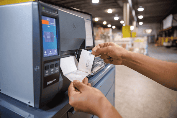 Worker removing a printed RFID label from a Zebra industrial printer in a warehouse
